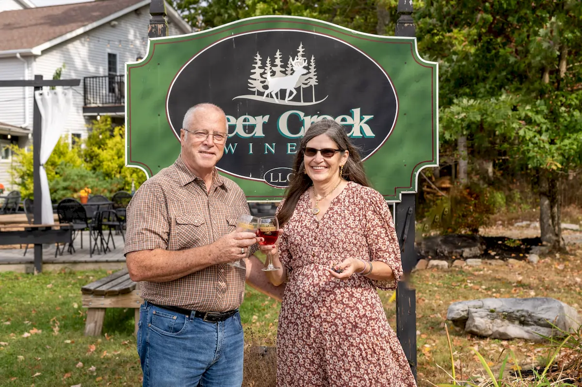 denny and rhonda brooks at deer creek winery at brooks estate in front of the deer creek sign cheersing glasses of deer creek wine
